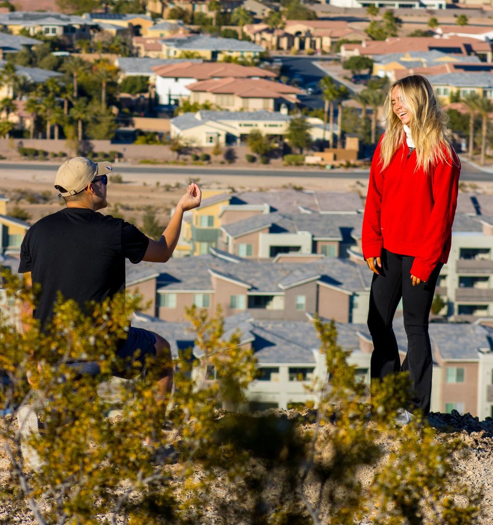 Man kneeling to propose to woman on a scenic hilltop overlooking Las Vegas suburbs.