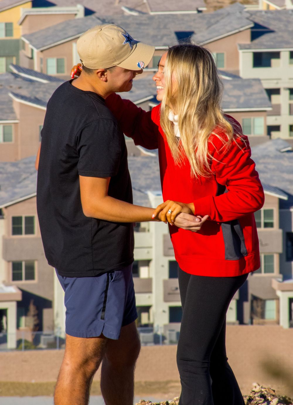 Smiling couple holding hands outdoors during golden hour with apartment buildings in background.