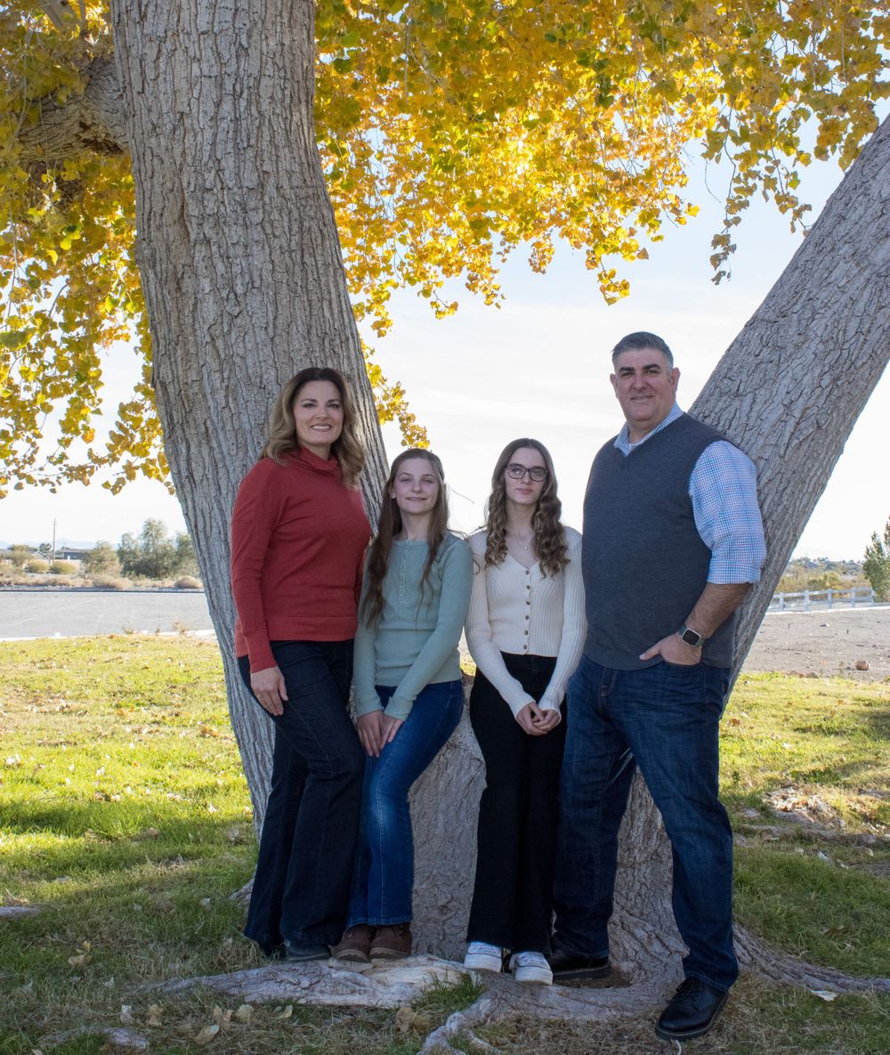 Family of four posing between large tree trunks with vibrant yellow autumn leaves in background.