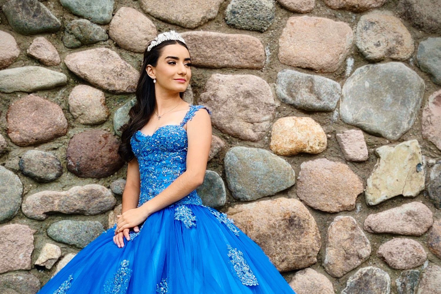 Royal blue quinceañera dress with beaded details against rustic stone wall background.
