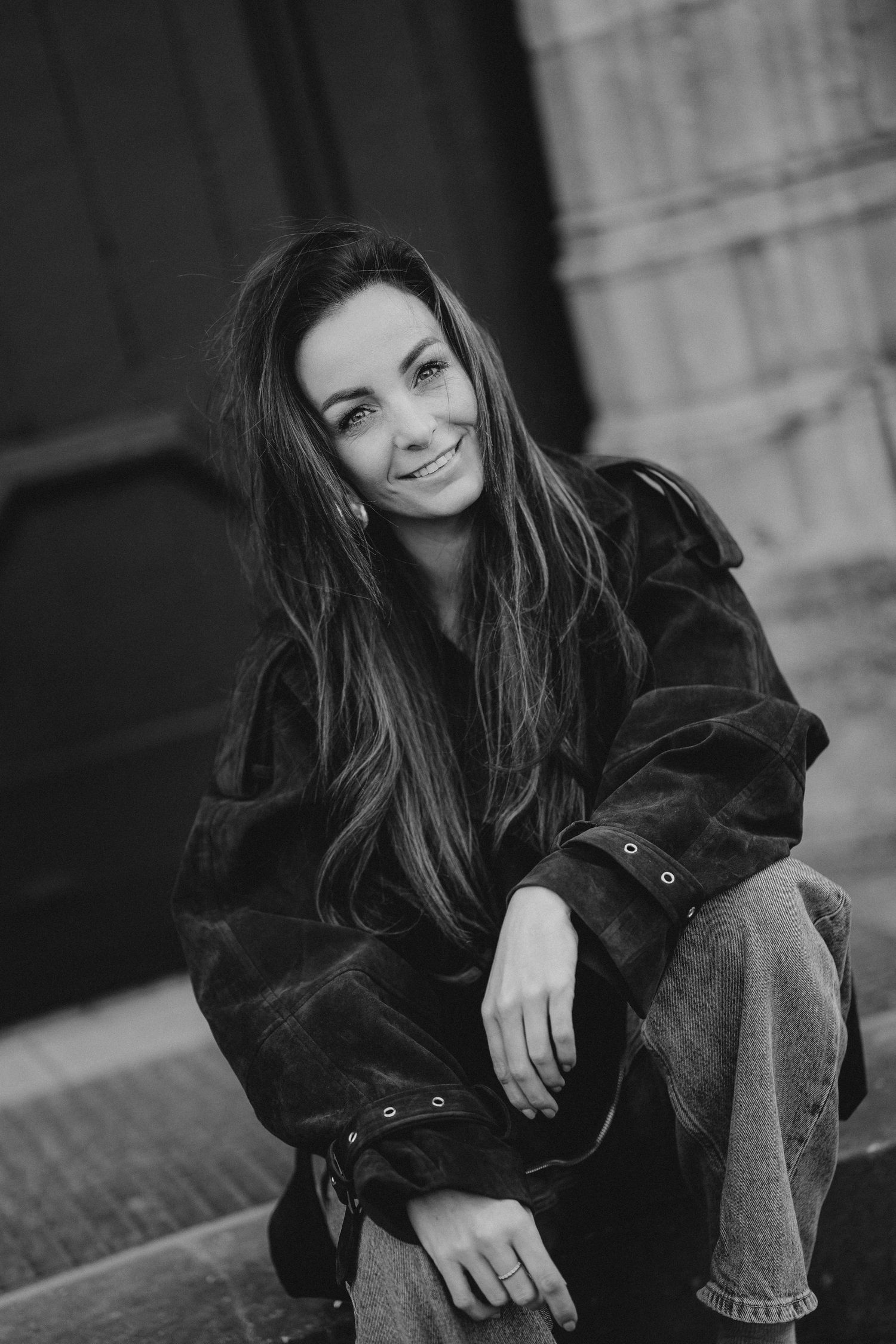 Casual portrait of woman in white shirt and jeans sitting with thoughtful expression.