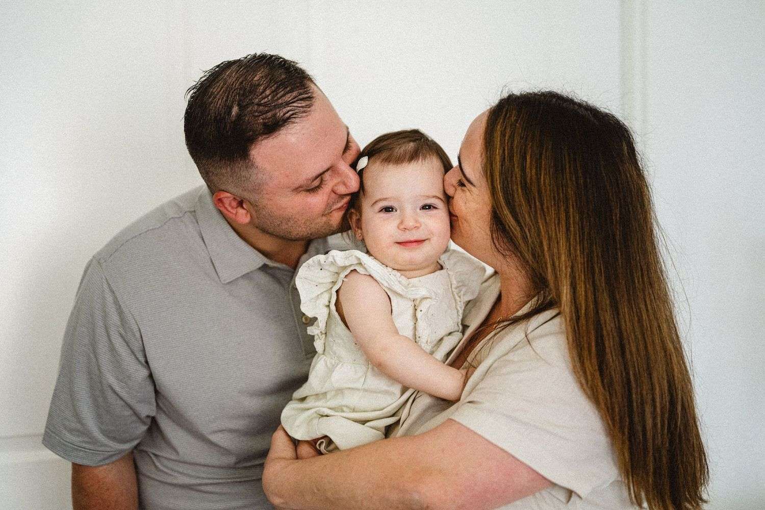Intimate family portrait against white wall showing affection with young child.