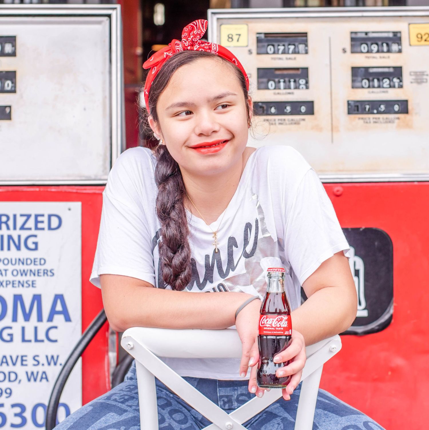 Young person in a white t-shirt and blue jeans sitting on a folding chair at a storefront.