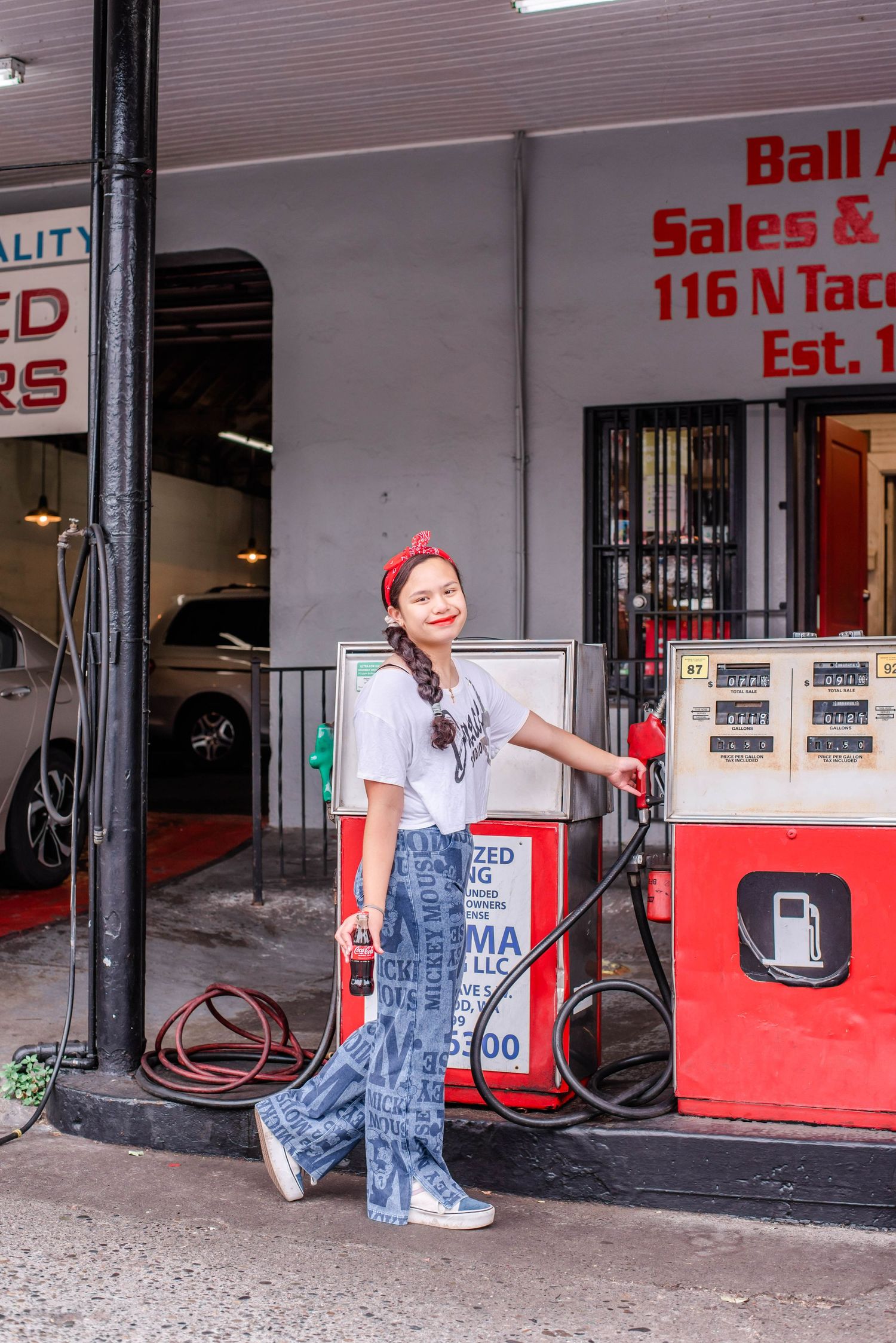 Person in casual wear poses by vintage gas pump outside Ball Sales building.