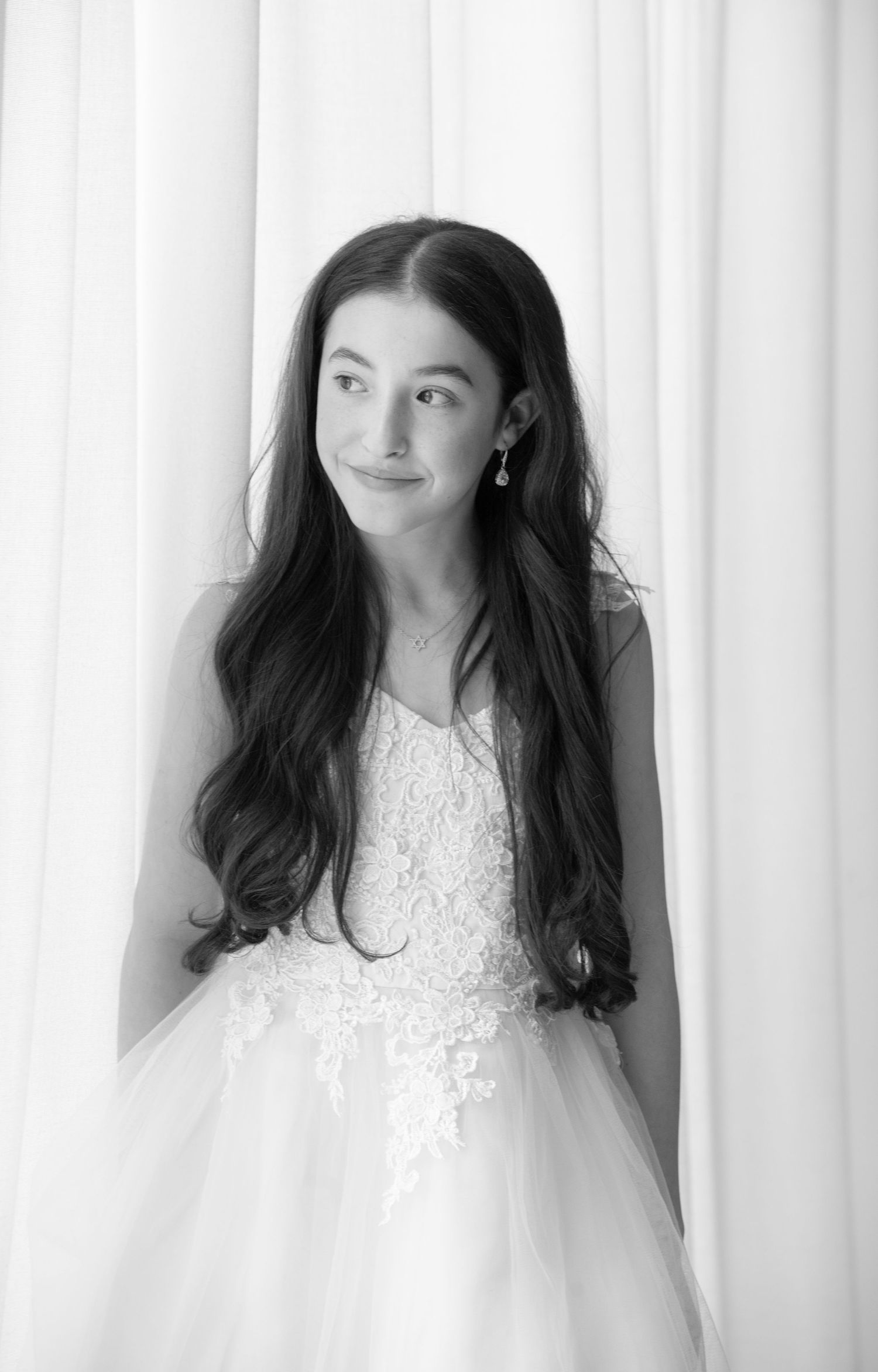Black and white portrait of someone in a white lace wedding dress with long dark hair against a light background.
