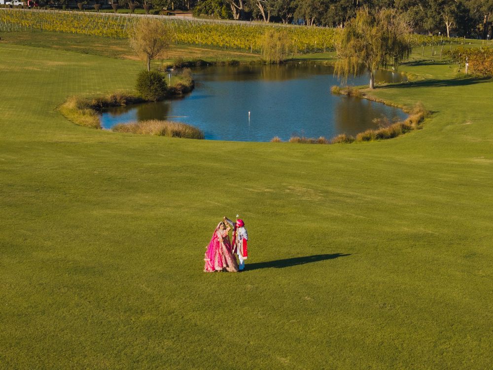 Couple in pink outfits walking on lush green golf course with scenic pond and willow trees in background.