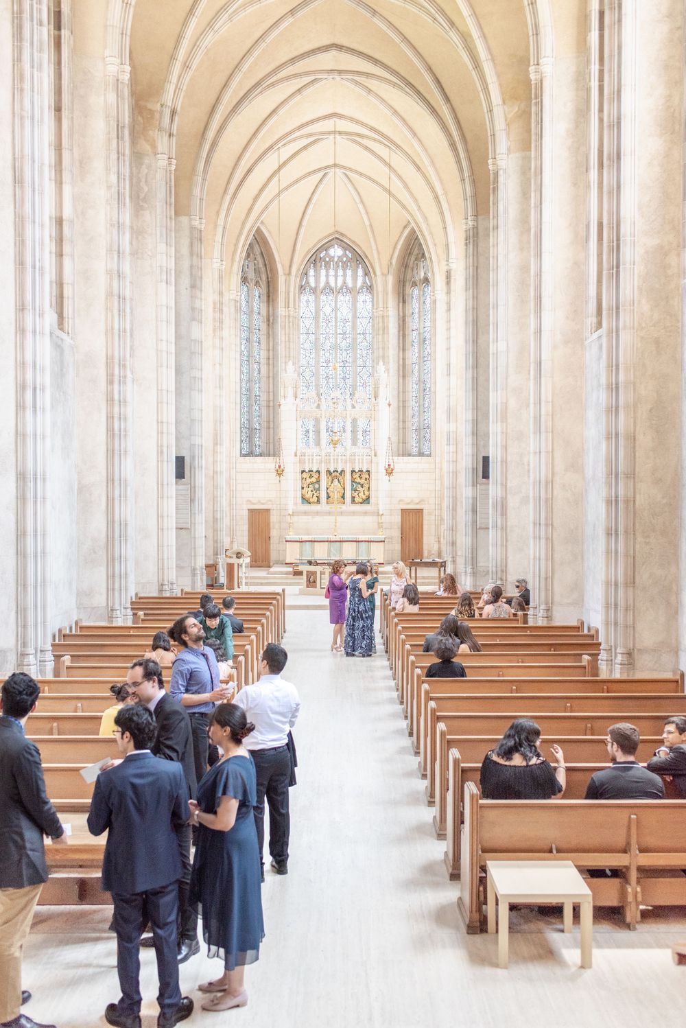 Interior view of the Gothic Trinity College Chapel with vaulted ceilings and pews, as guests gather before the wedding ceremony.