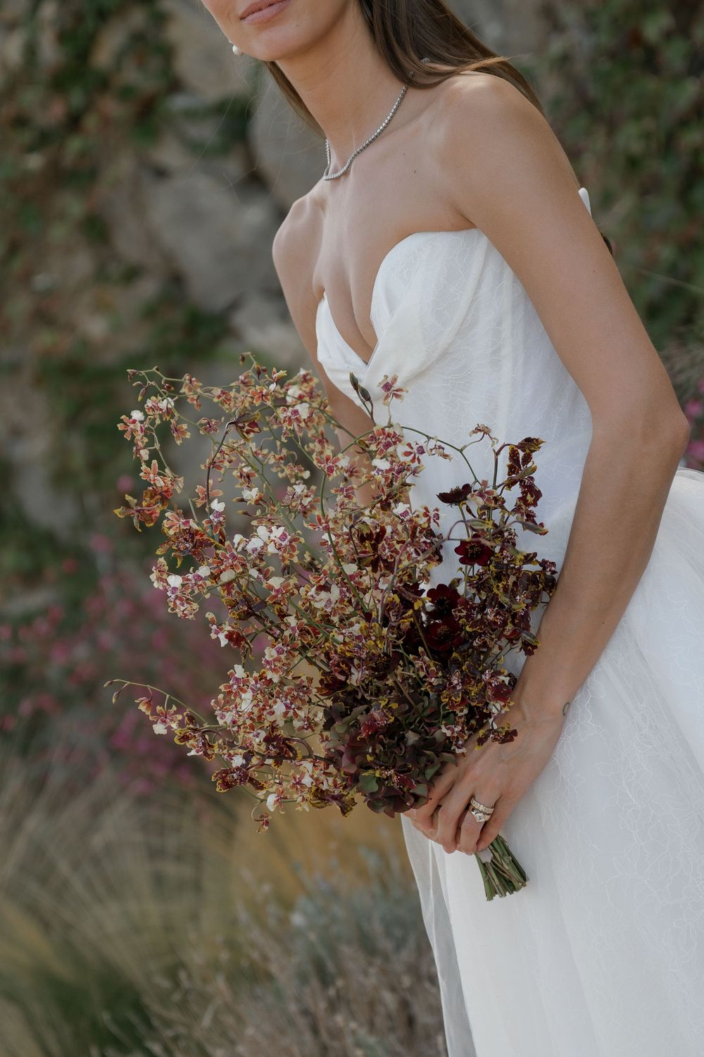 A delicate dried floral bouquet is held against a white strapless wedding dress in an artistic bridal portrait.