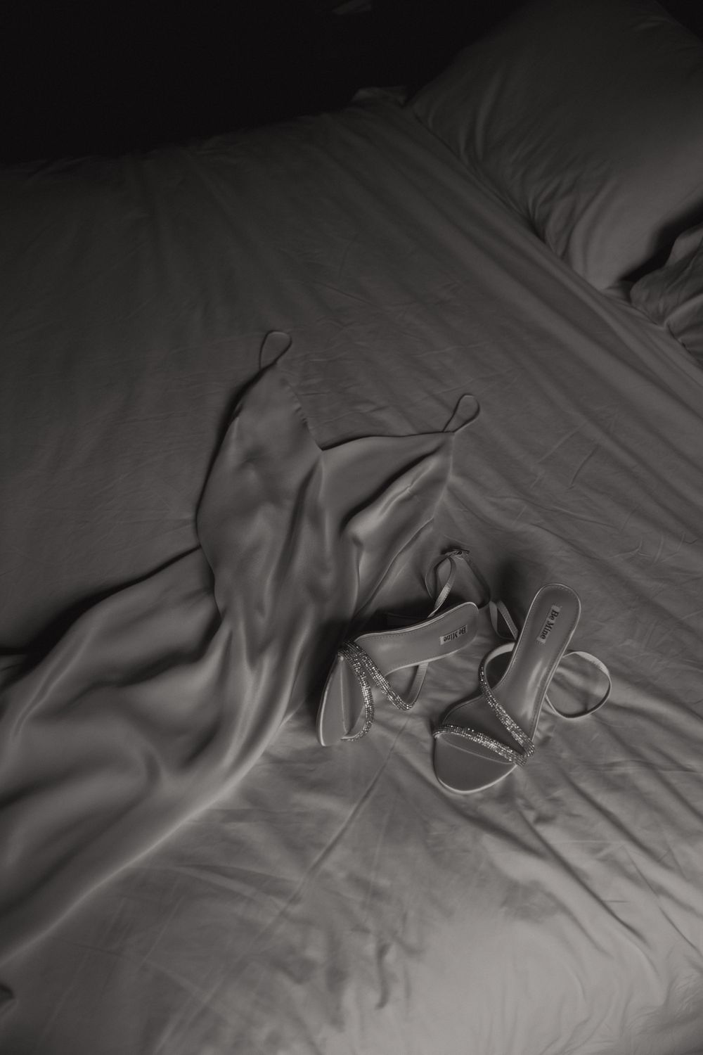 A black and white close-up photo shows rumpled bedsheets with soft shadows creating abstract patterns and textures.