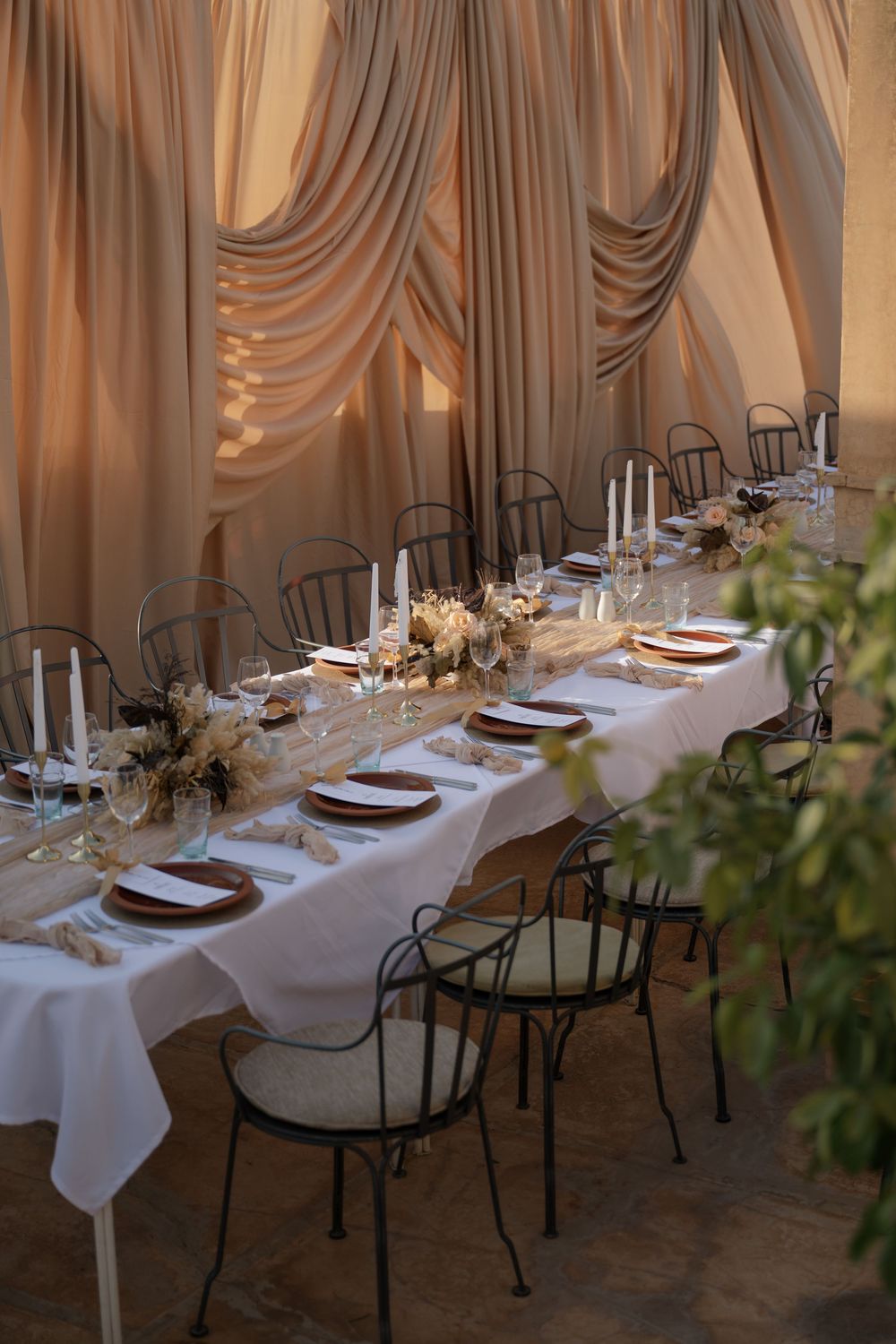 Elegant dining table setup with white linens, metal chairs, and draped fabric decor for an intimate gathering.