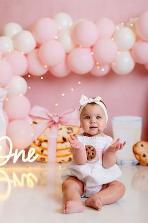 Pink and white balloon arch creates a dreamy backdrop for a baby's first birthday celebration setup with cookies and decor.