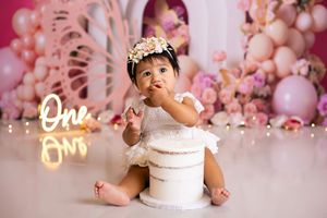 Pink and white cake smash photography session with balloons and floral decorations for first birthday celebration.