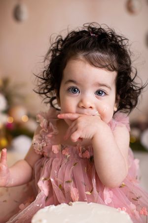 Baby in pink dress smiles while putting fingers in mouth in series of connected photos.