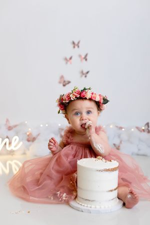 A cake smash photo session featuring a white cake, pink tulle dress, and delicate butterfly decorations in a dreamy setting.