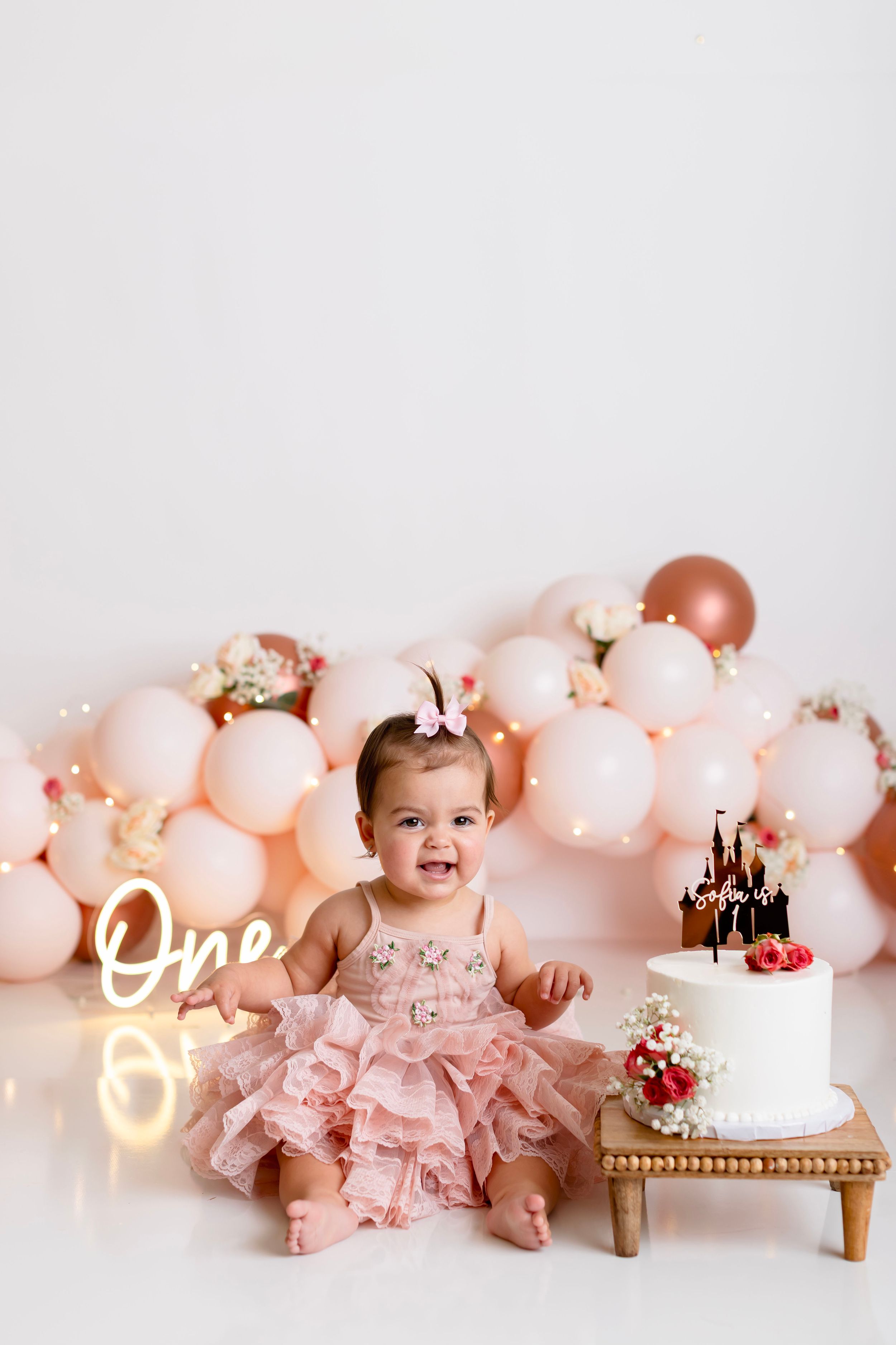 Pink balloon garland and decorative cake setup for a first birthday celebration with soft romantic lighting.