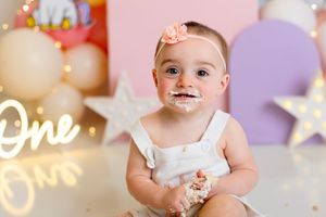 First birthday cake smash photo session with pastel decorations and glowing lights in the background.