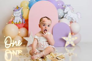 Pastel balloons and unicorn decorations create a magical first birthday cake smash scene with gold glitter.