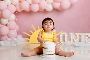 First birthday cake smash session with yellow ONE sign and pink balloon garland backdrop.