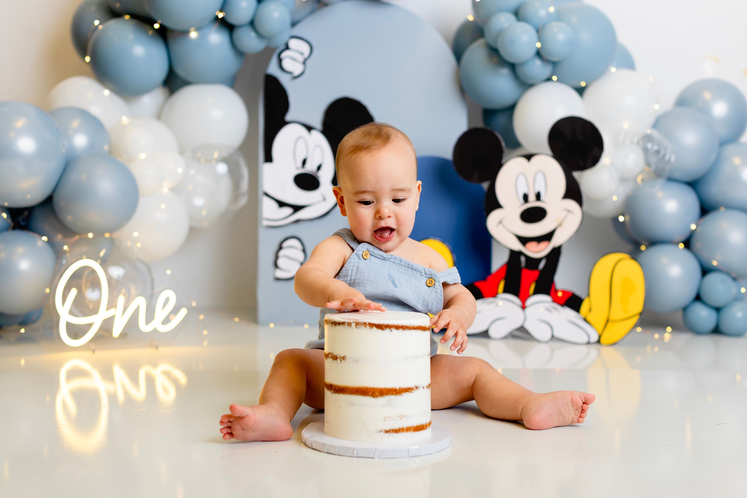 Blue and white balloon arch decorates a Mickey Mouse themed first birthday cake smash photo session backdrop. Family NJ photographer