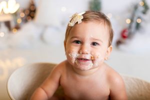 Smiling baby with cake frosting on face during first birthday photoshoot with bokeh lights in background.