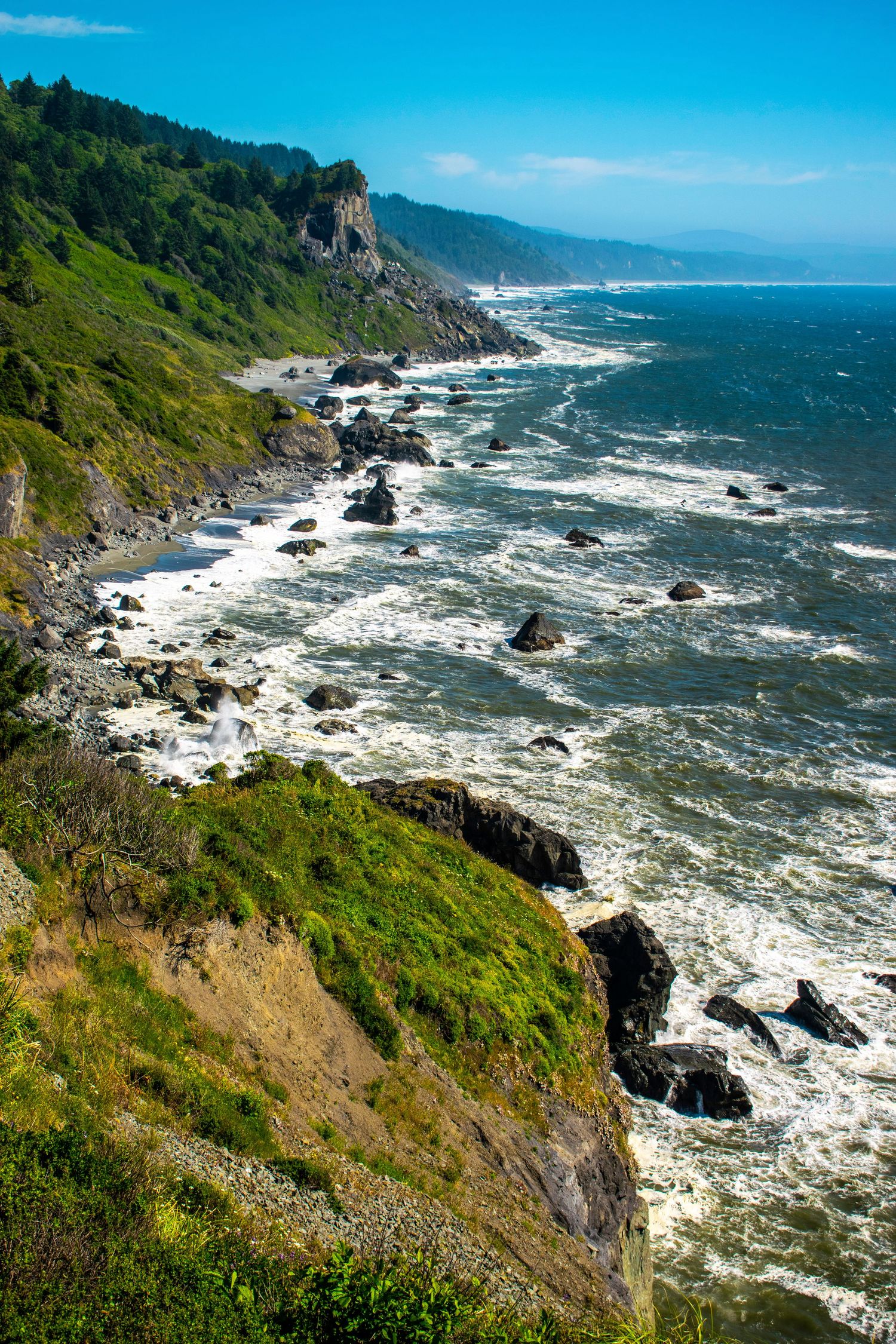 Rugged Pacific coastline with dramatic cliffs and crashing waves against rocky shore.