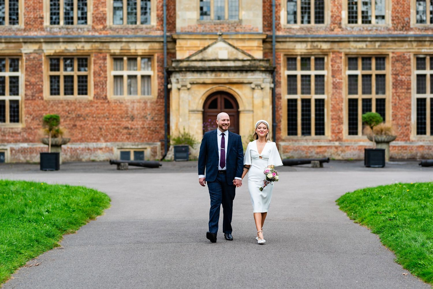A couple walks together on a path in front of a historic brick building with ornate architecture.
