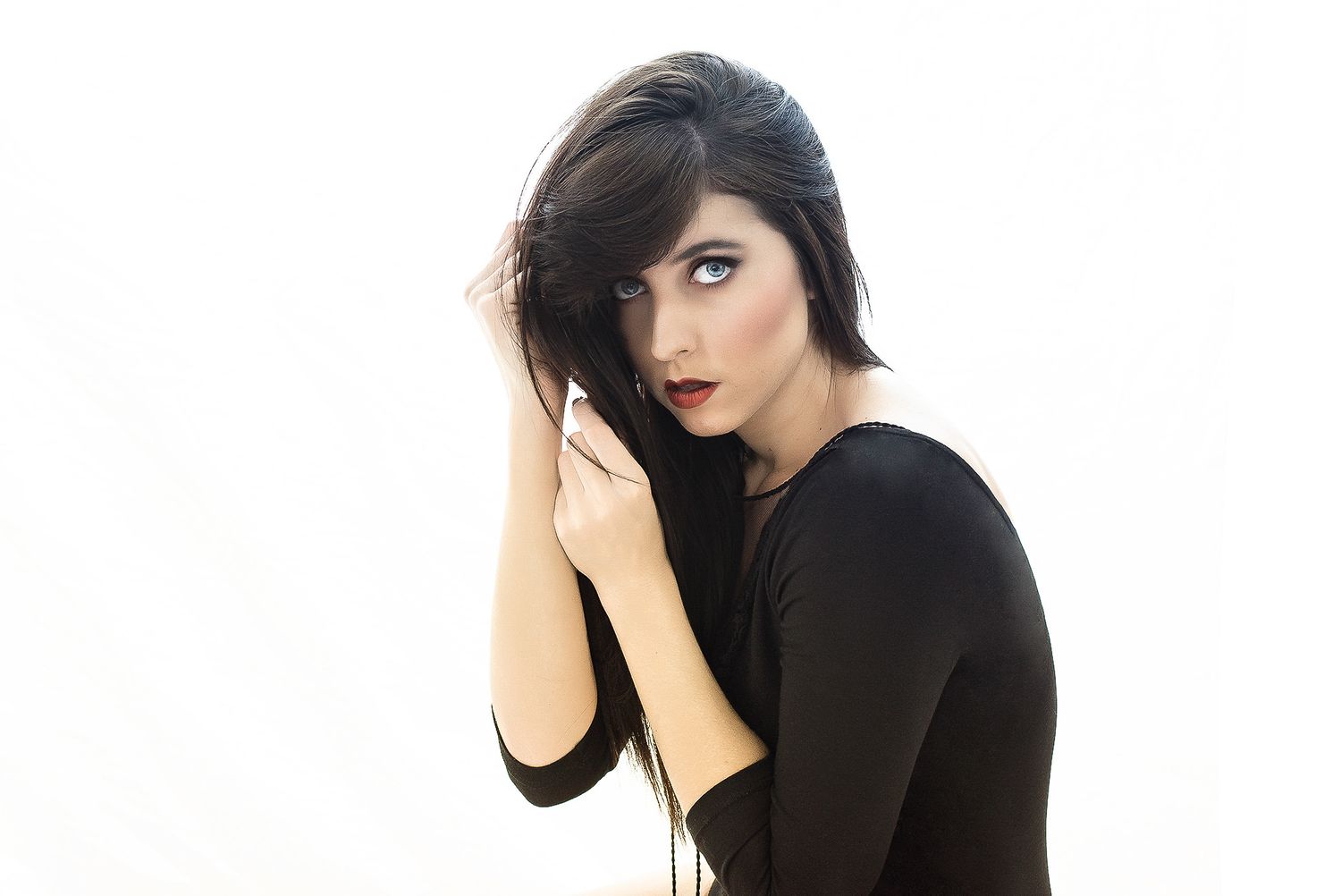 Brunette woman in black outfit with short hair and bold red lips against white background.