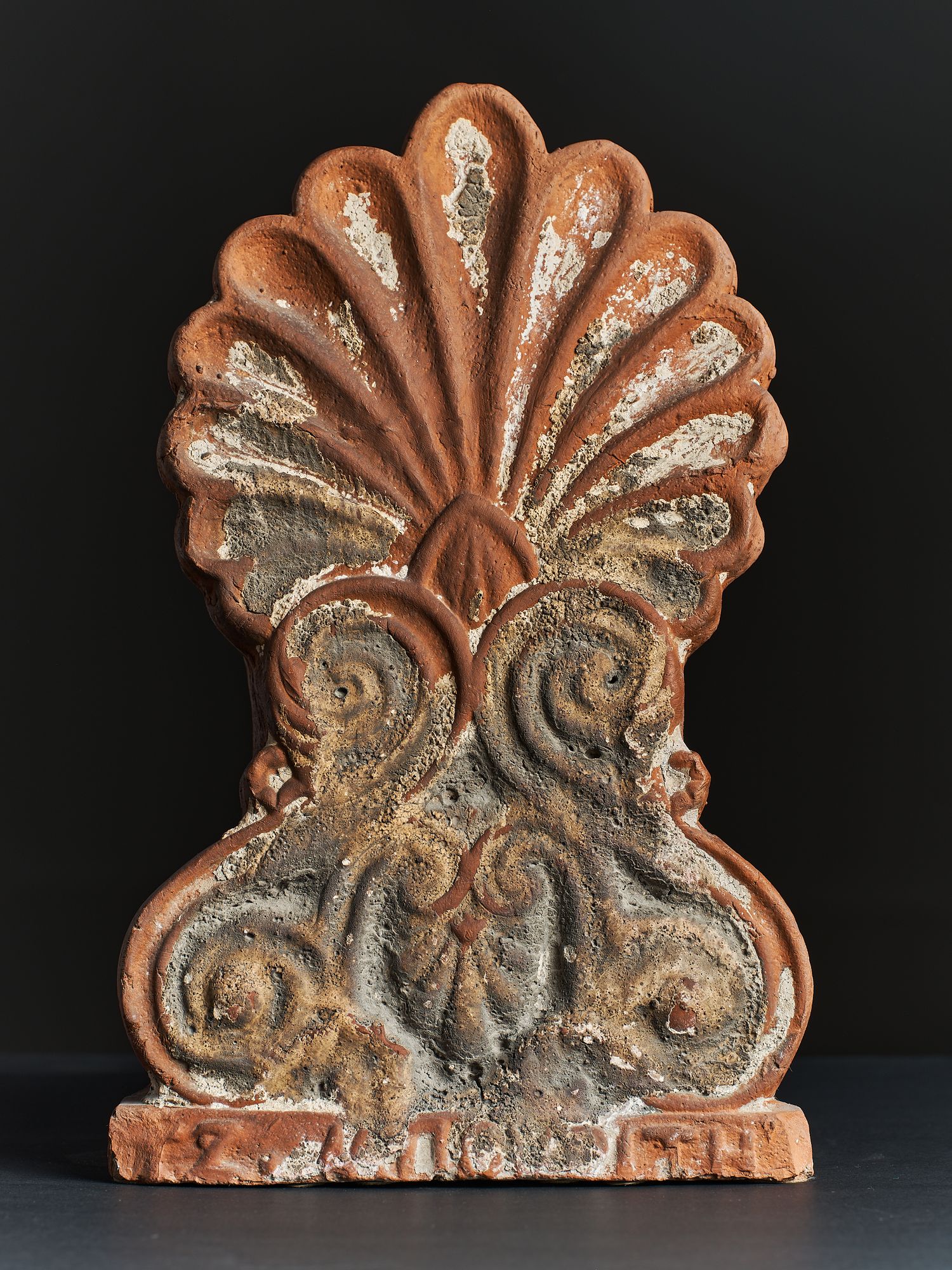Antique terracotta architectural finial with fan-shaped top and ornate scrollwork relief details, showing aged patina.