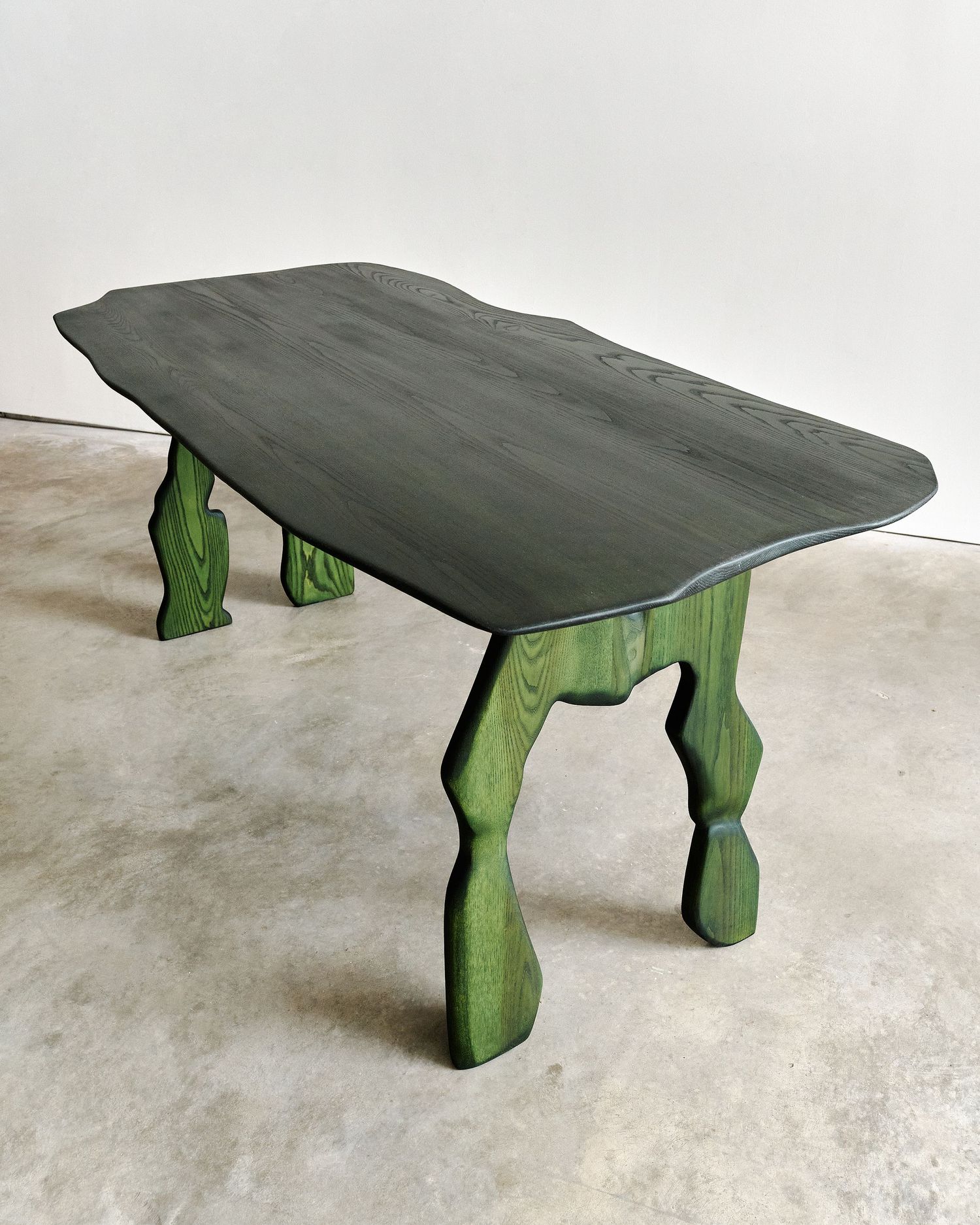 Dark green wooden table with sculpted organic legs and a live-edge top, handcrafted artisan furniture piece.