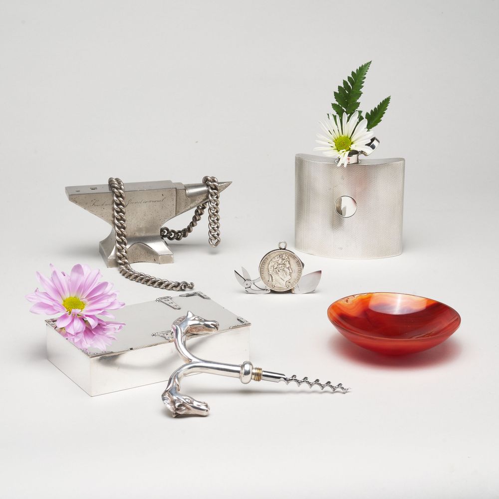 Elegant table setting with silver accessories, pink flowers, and red dish on white background.