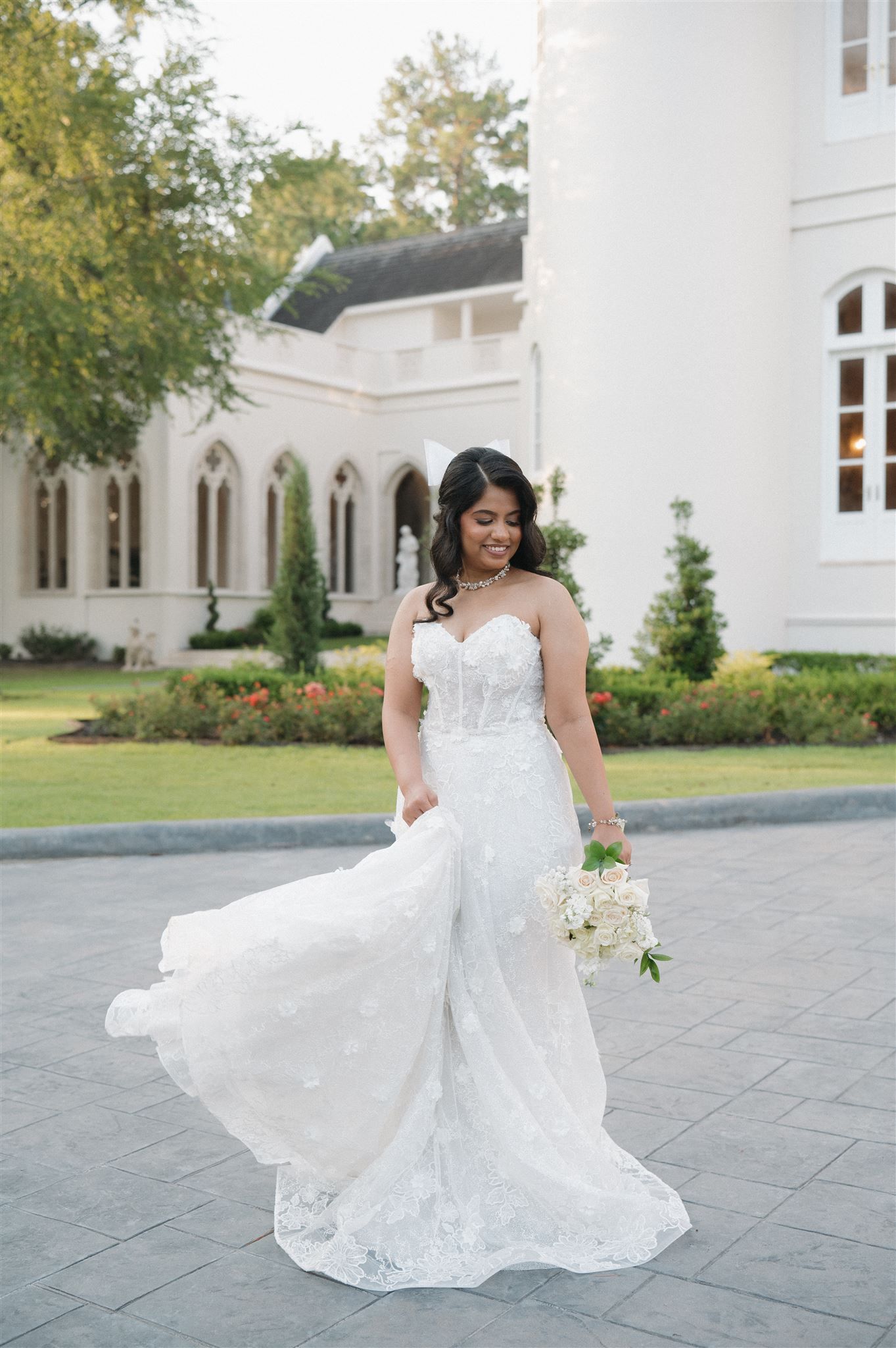 A stunning wedding dress with intricate lace details and flowing train photographed outside a white Gothic-style church.