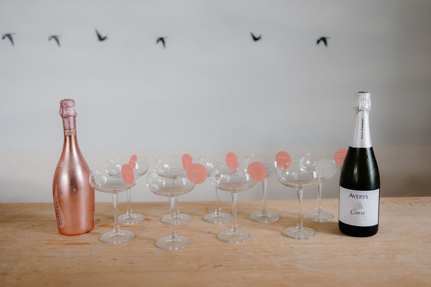 Rose gold and traditional champagne bottles with empty glasses arranged on a wooden table.