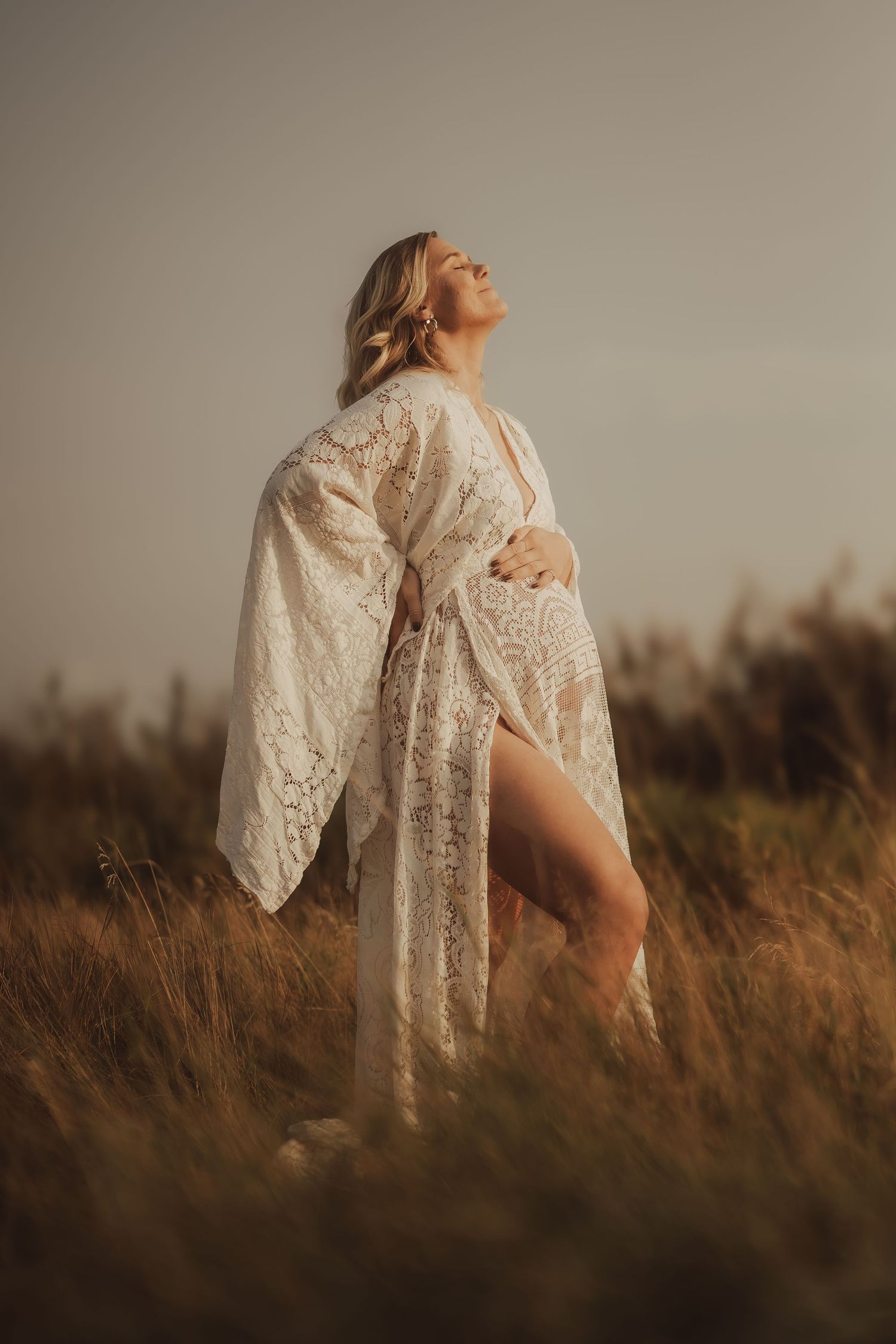 A person in a flowing floral embroidered gown poses on a beach at sunset with warm golden tones.