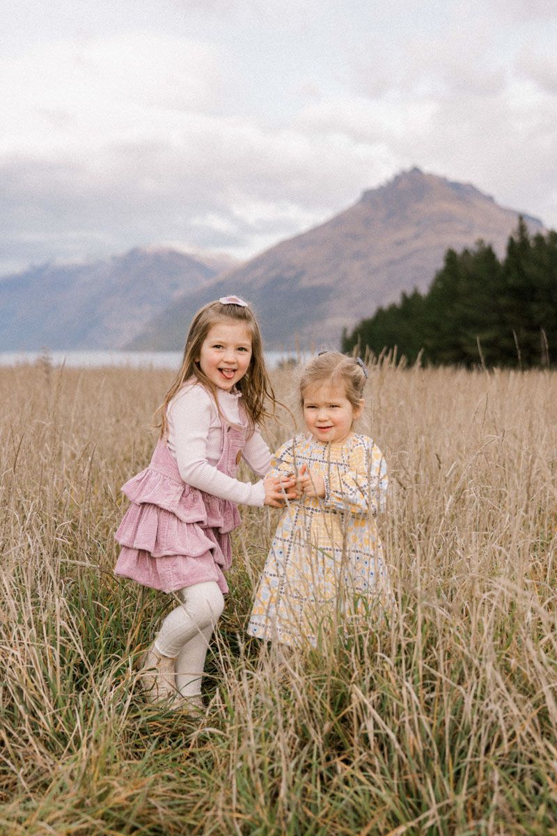 Children playing and running through tall grass field with mountains in background.