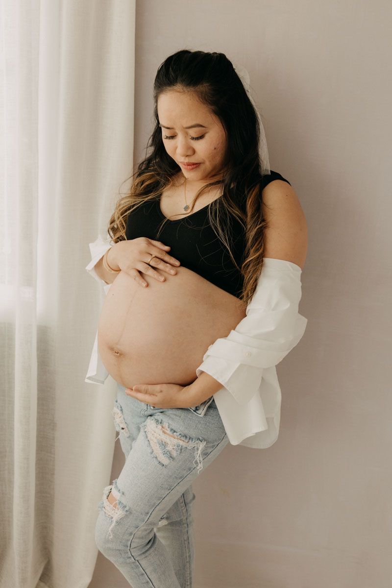 Maternity photo series showing expecting mother in casual outfit against white curtain backdrop.