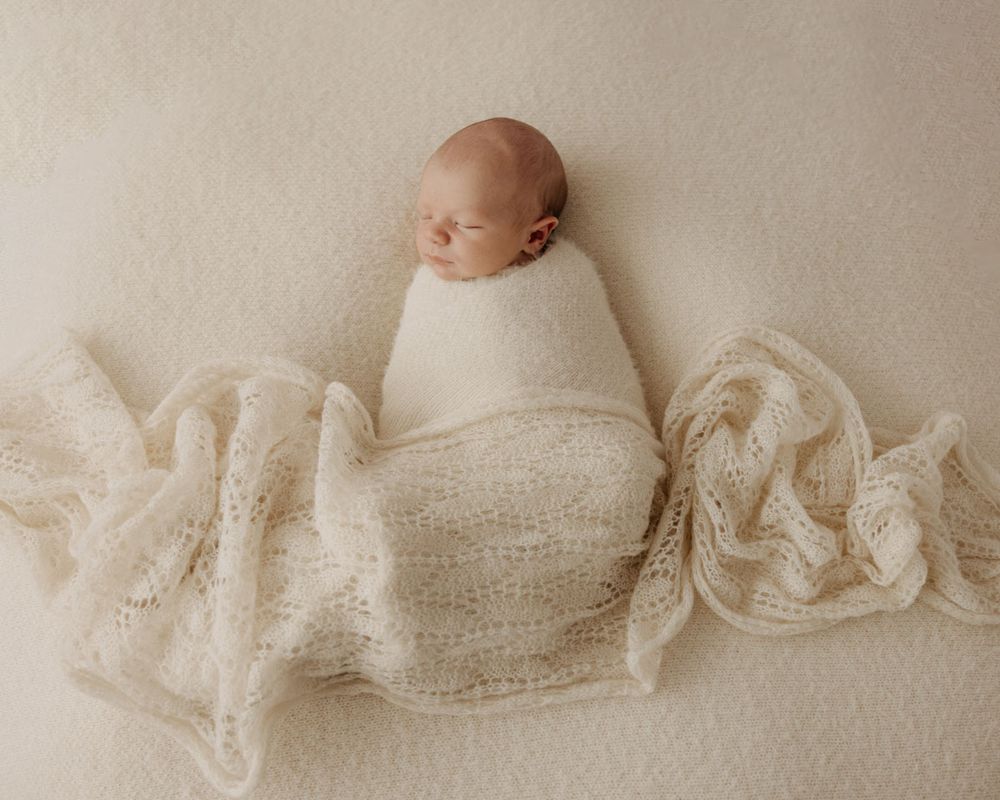 Neutral toned newborn photography setup with white fabric draping across frame.