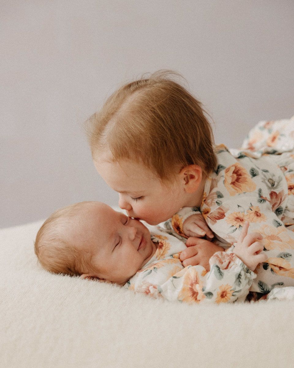 Siblings in floral outfits resting together during intimate indoor photo session.