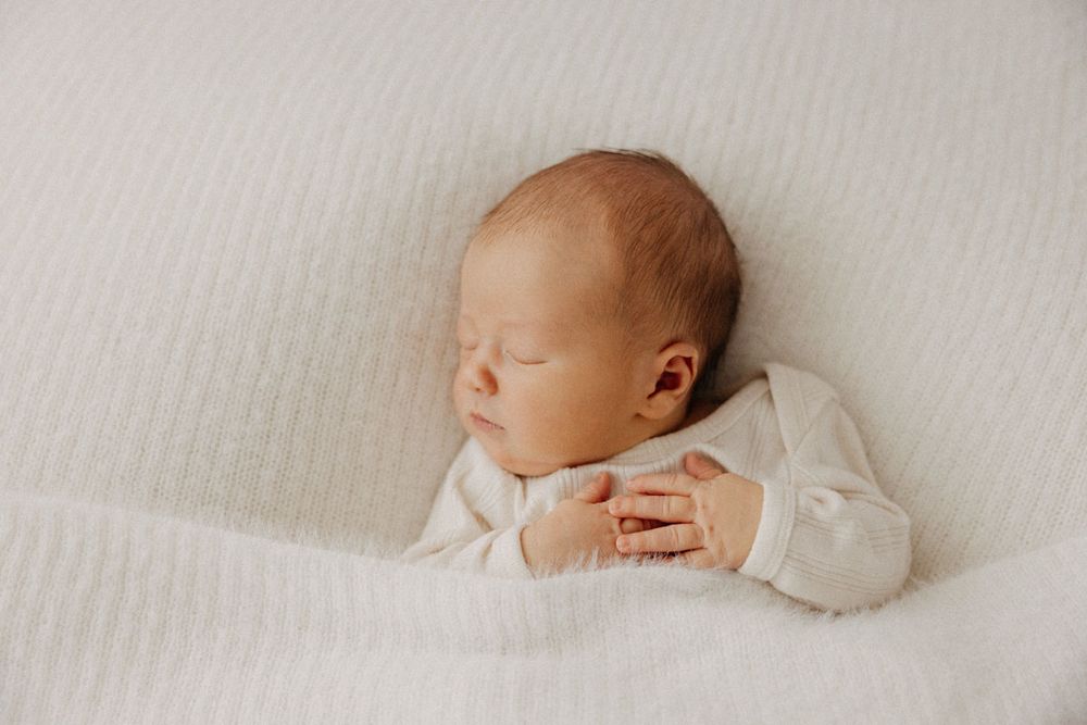 Peaceful sleeping newborn in white onesie rests on textured white blanket.
