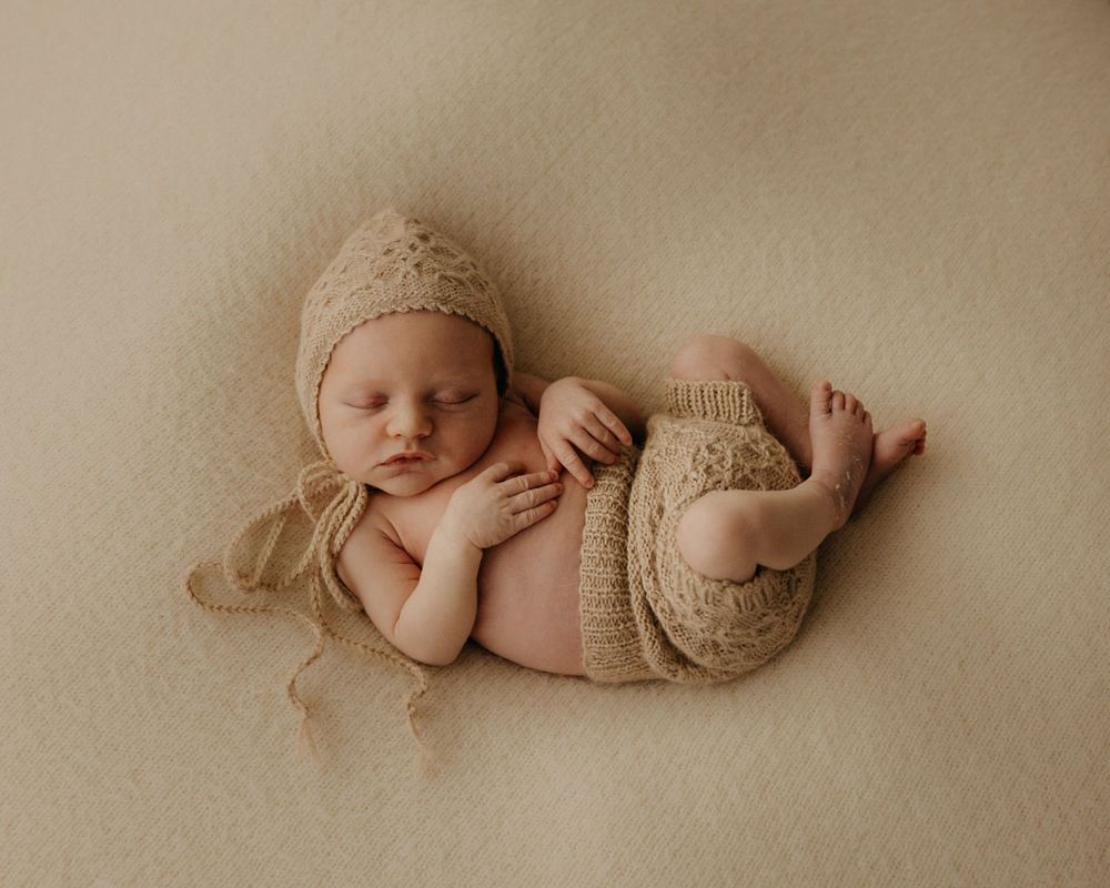 Newborn baby sleeping peacefully in cream knit wrap during minimalist studio session.
