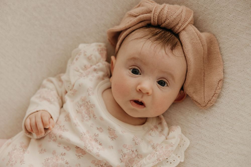 Infant wearing soft lace clothing rests on beige background in gentle studio lighting.