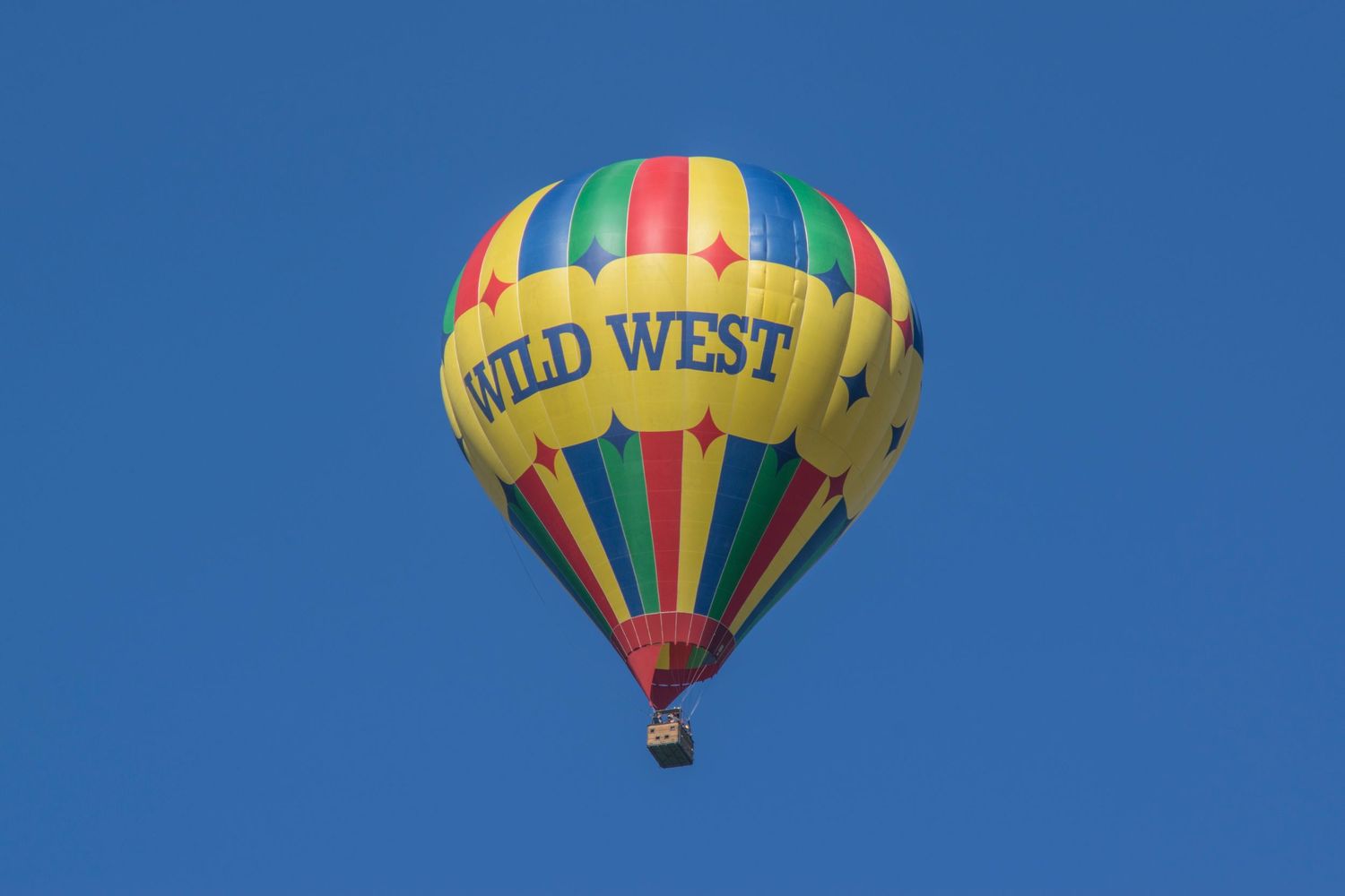 Colorful 'Wild West' hot air balloon floating in bright blue sky.
