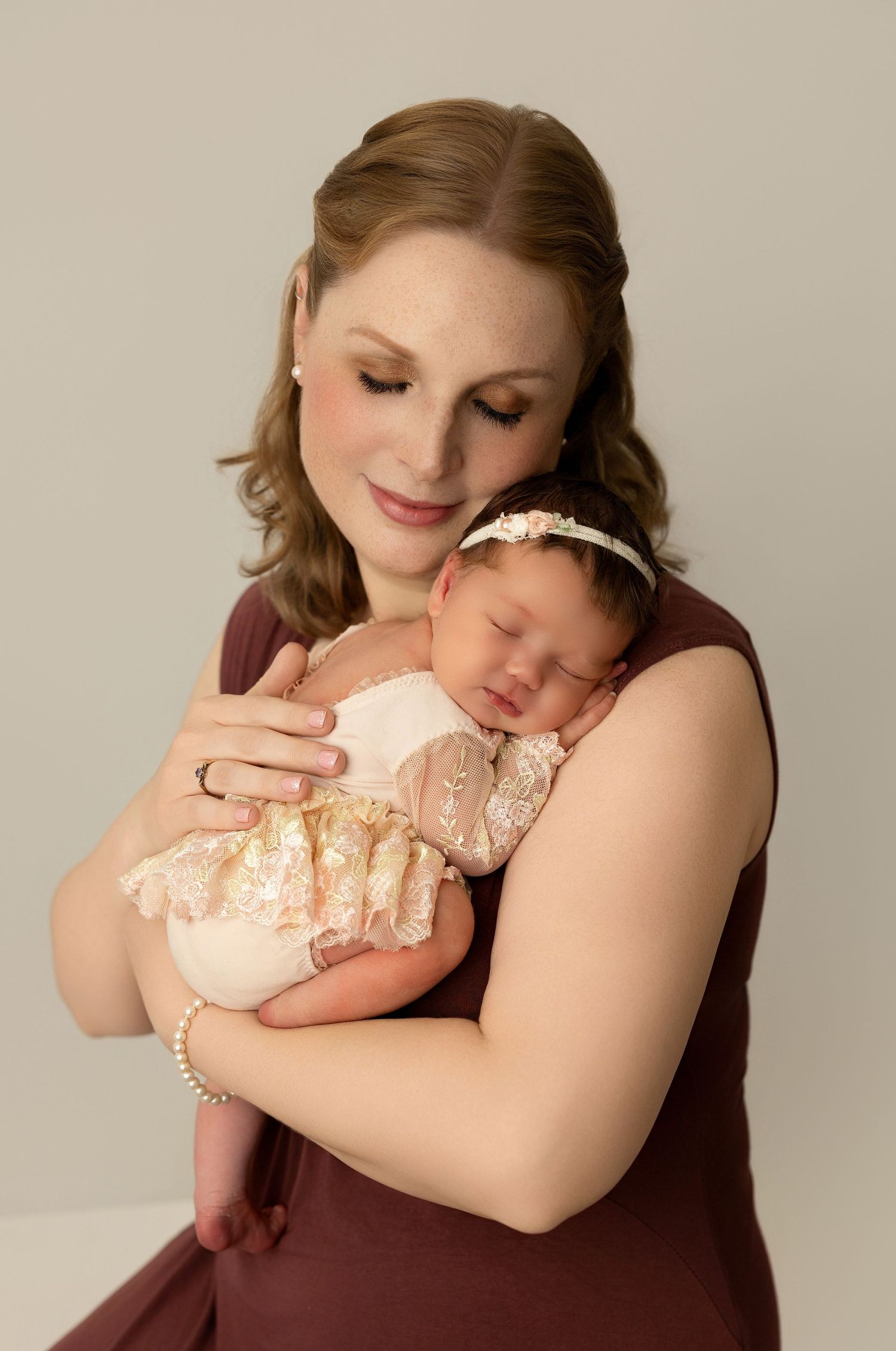 Tender photograph series showing parent holding sleeping baby in peach dress against soft neutral background.