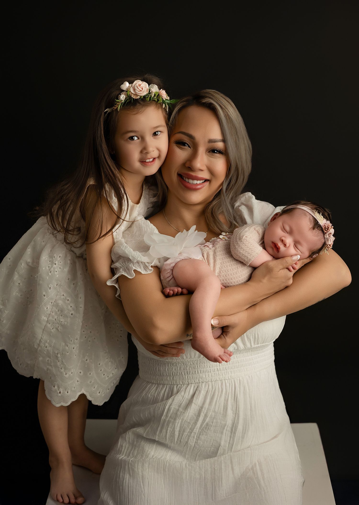 A tender family portrait series in white dresses against a dark background shows intimate moments between parent and children.