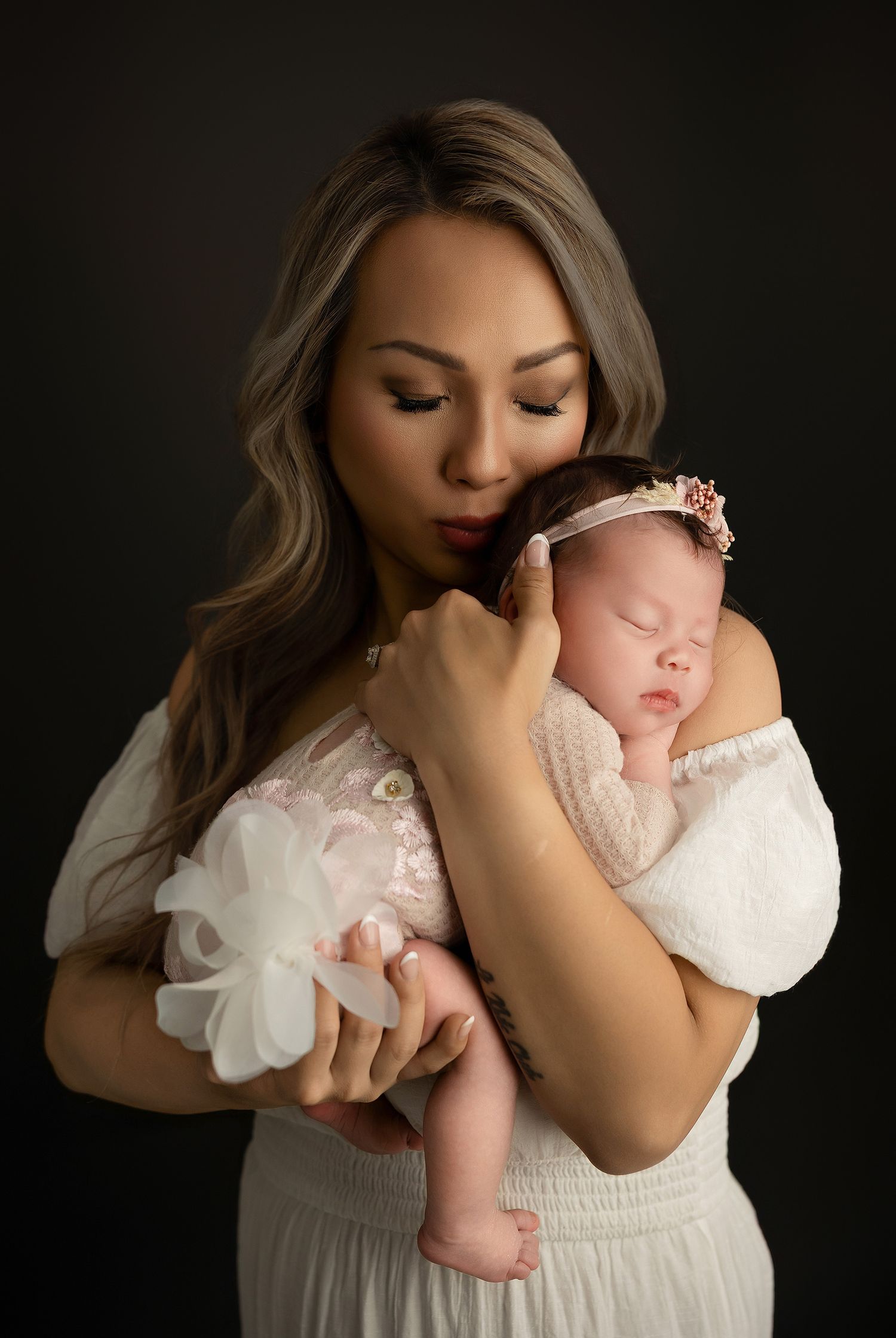 Artistic black and white portrait series capturing intimate maternal moments in white clothing against dark backdrop.