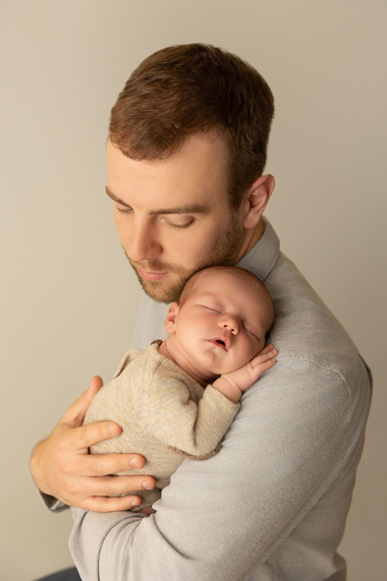 Intimate portrait series showing parent cradling sleeping infant in grey clothing against neutral background.