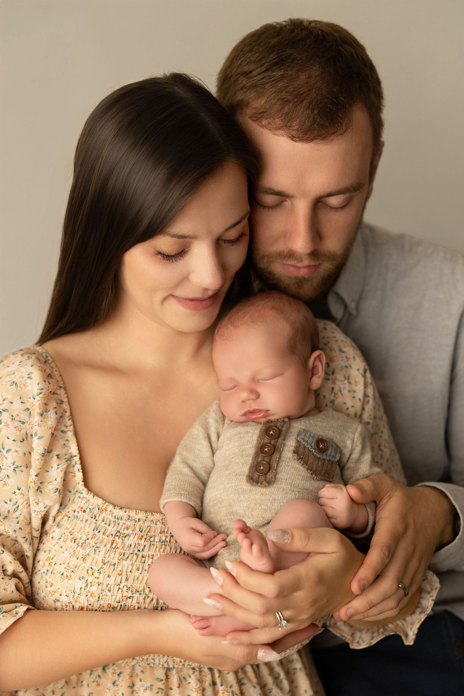 Sweet family portrait showing parents cradling sleeping newborn baby in beige tones.