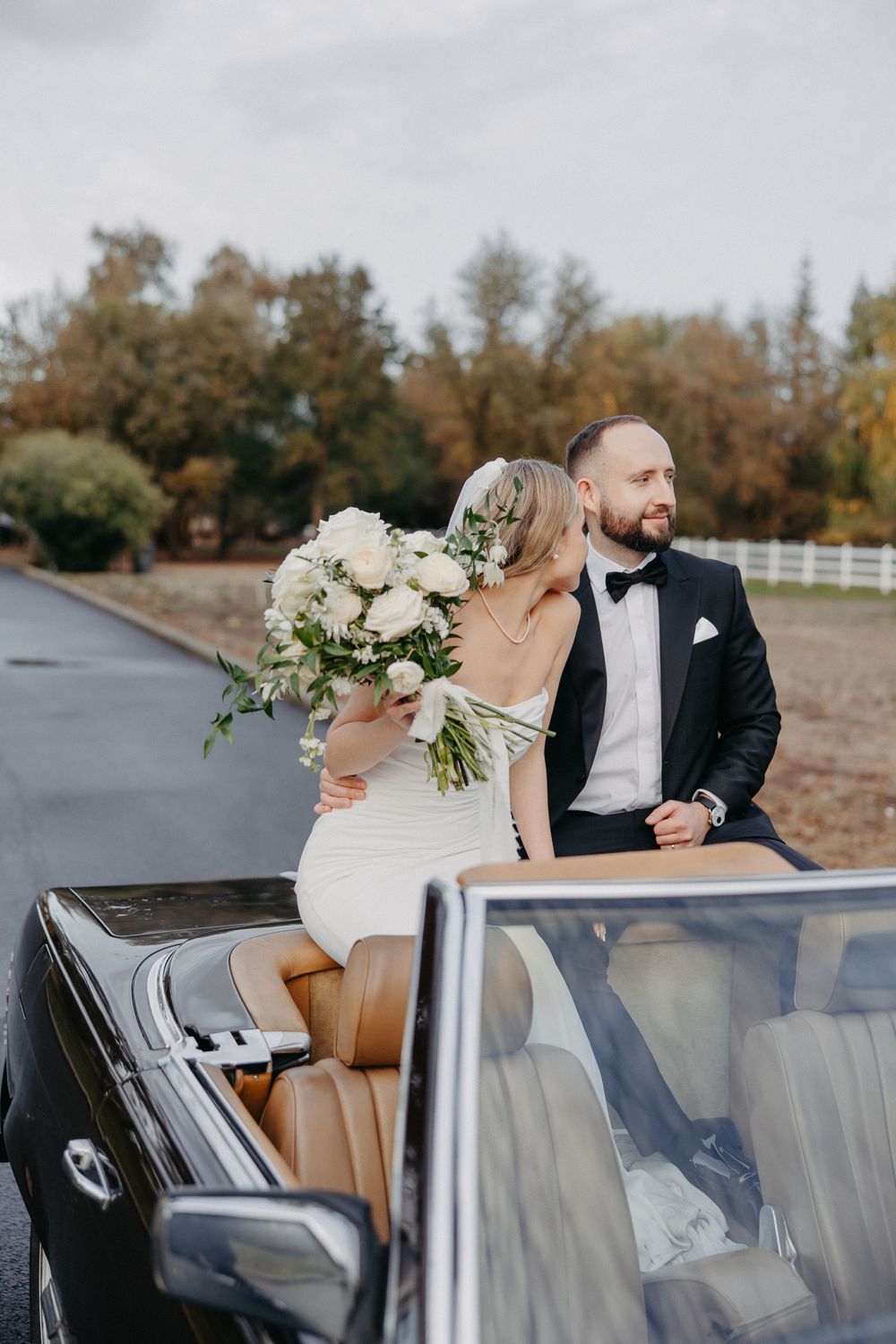 Couple with vintage convertible Mercedes in autumn setting with white floral arrangements.