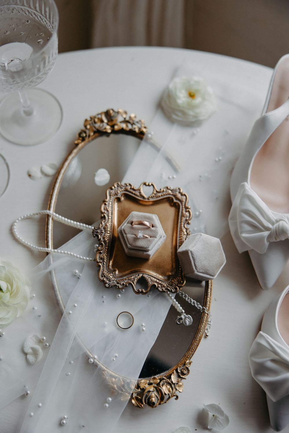 Wedding accessories including rings and shoes arranged on an ornate vintage mirror tray.