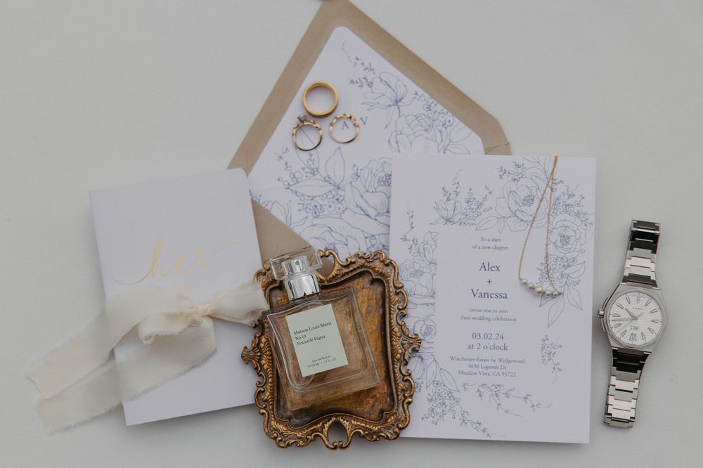 Wedding details with invitation, rings, watch and decorative gold frame on light background.