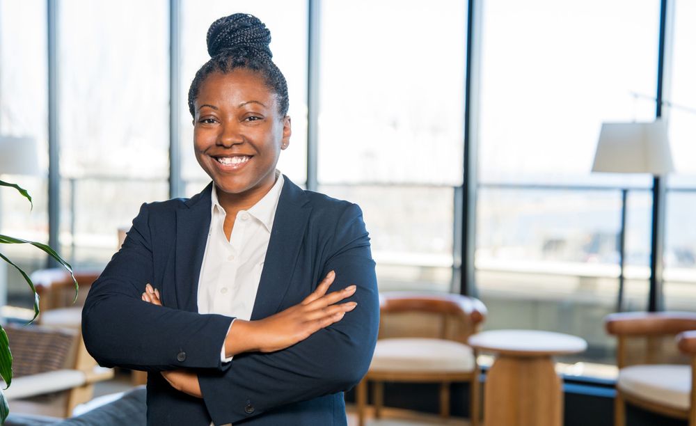 Professional in a dark blazer sits at a modern office desk with a warm, welcoming expression.
